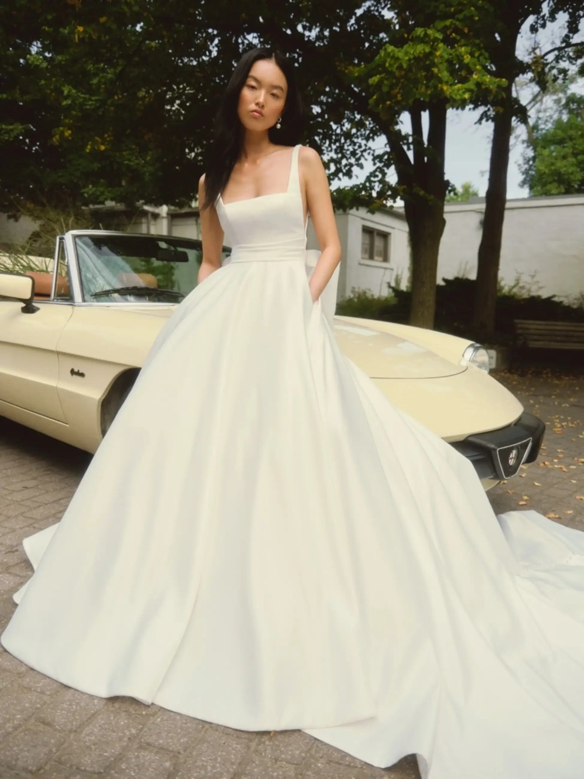Model is wearing a satin ball gown with a back bow and square neckline