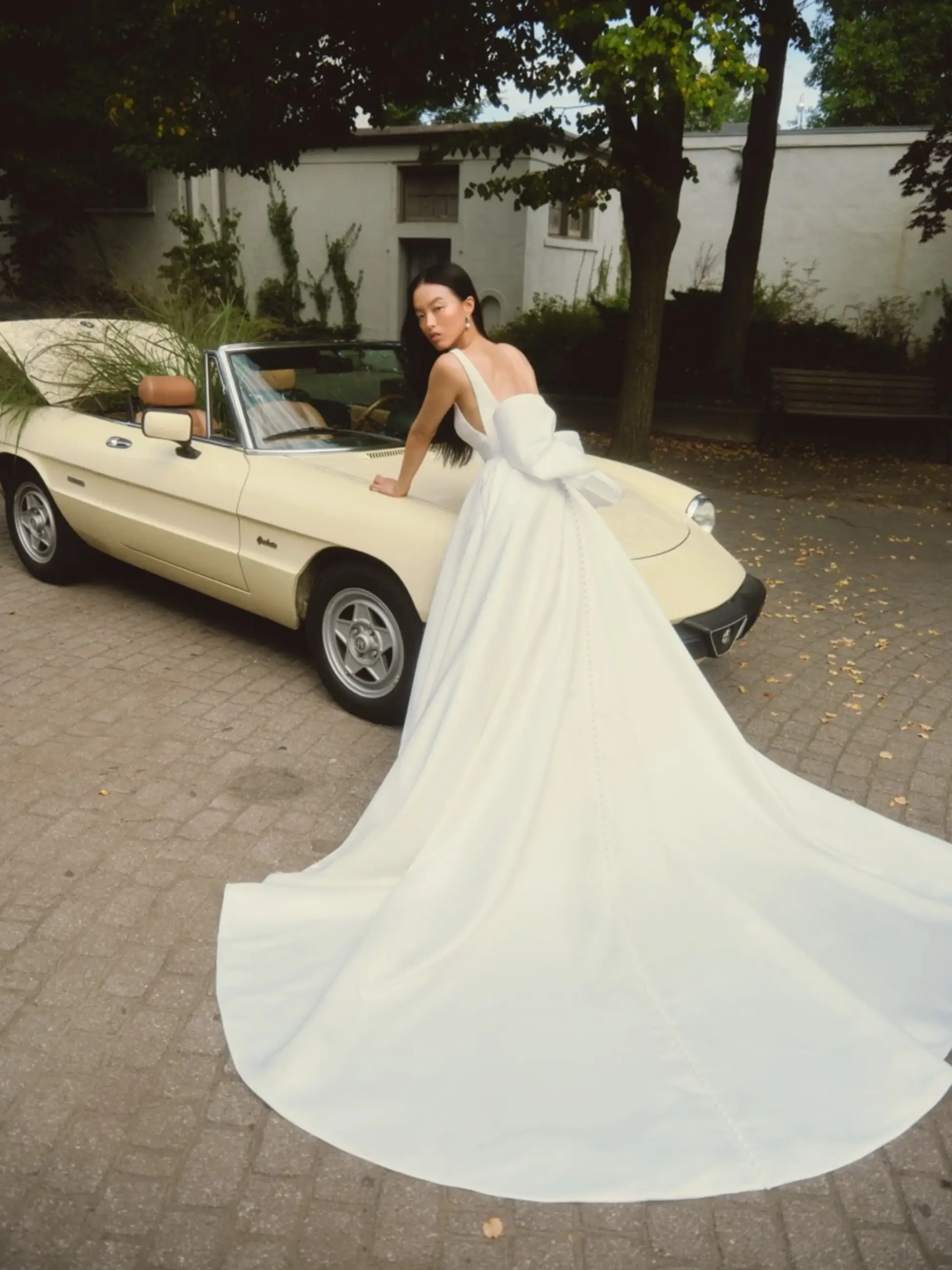 Model is wearing a satin ball gown with a back bow and square neckline