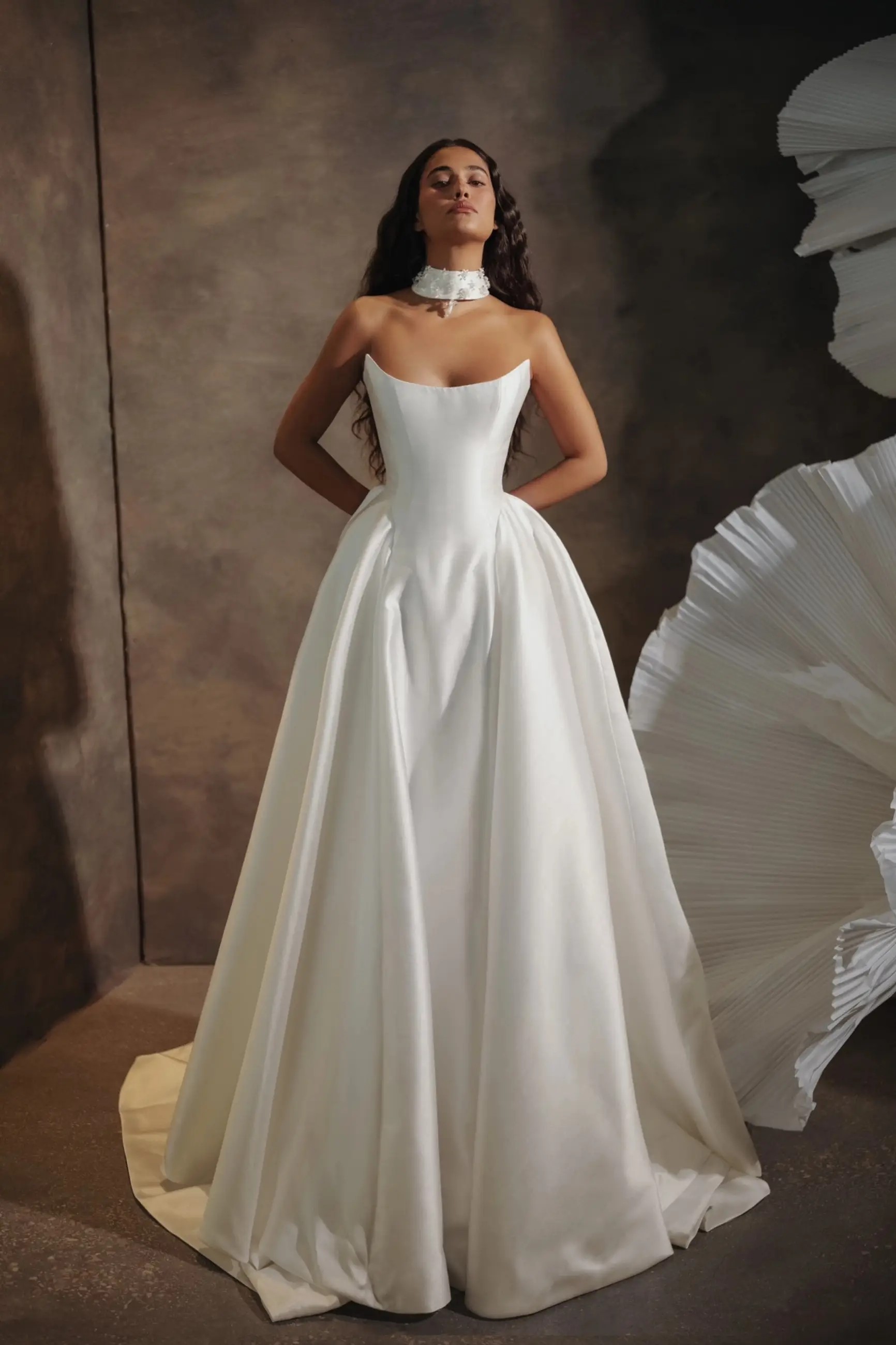 Model is wearing a strapless ball gown wedding dress with a basque waist and sleek fabric