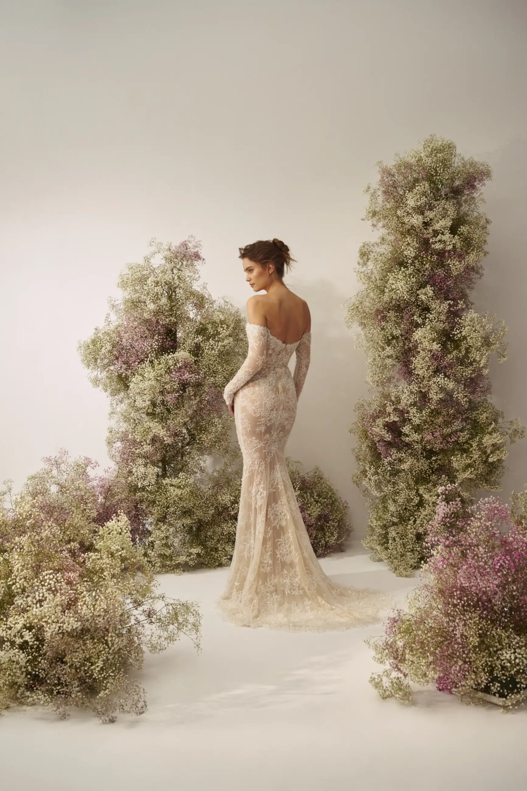 Model is wearing a fitted lace gown with an off-the-shoulder sweetheart neckline, beaded long sleeves, and a detachable silk overskirt.