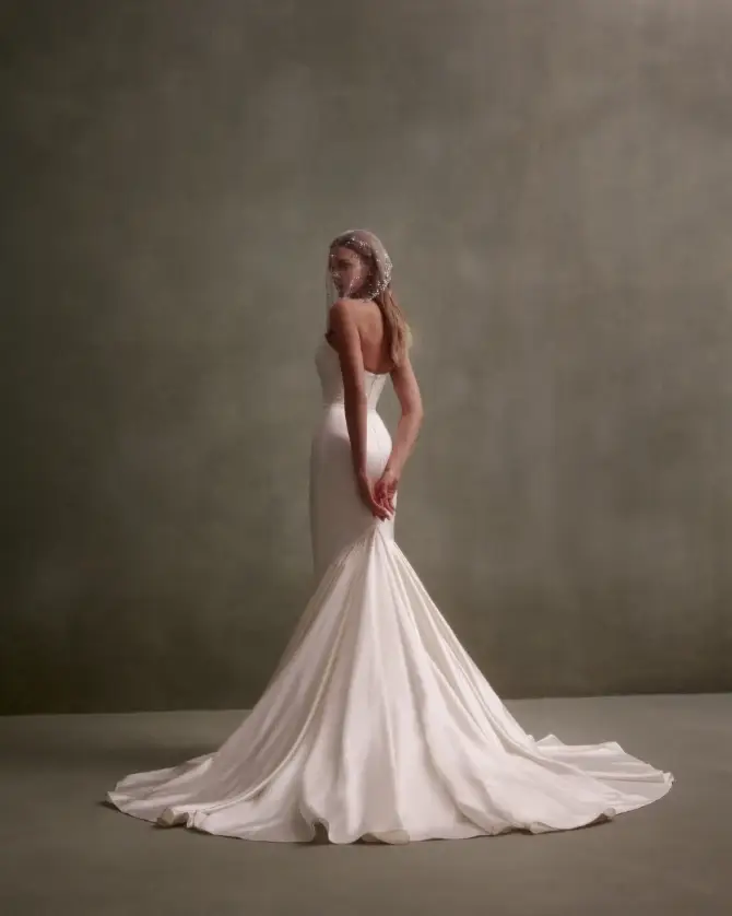 Model is wearing a satin mermaid bridal gown with a strapless scoop neckline