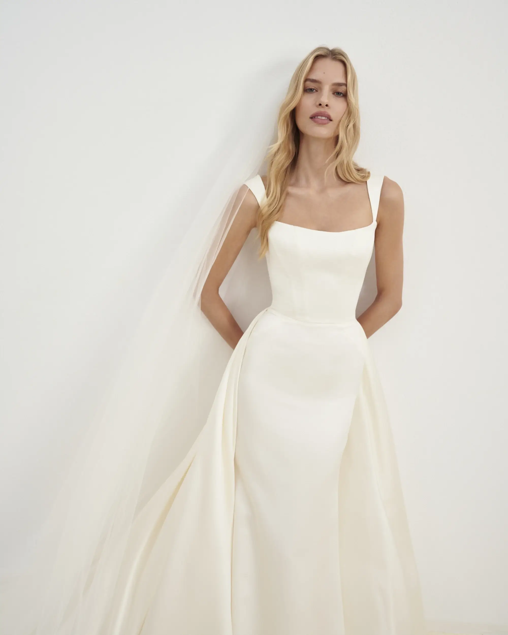 Model is wearing a fit-and-flare satin dress with tapered straps, a square neckline, and an exaggerated pleated panel train crafted from Silk Mikado