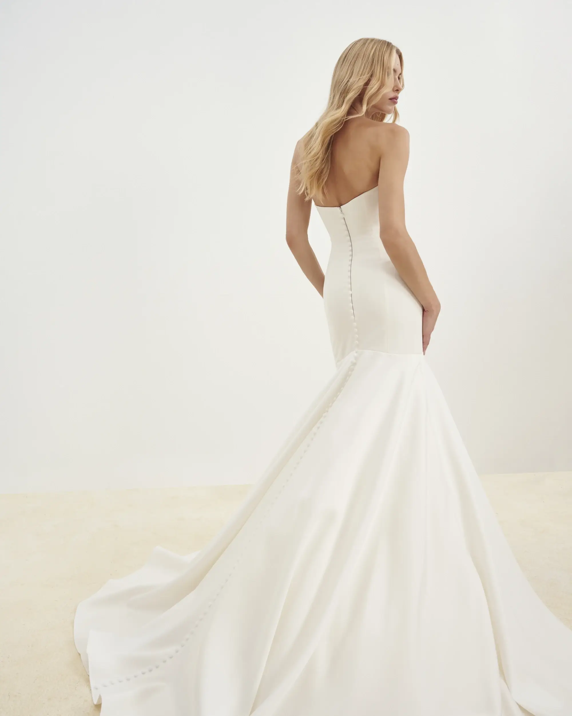 Model is wearing a strapless mermaid gown featuring elegant button detailing down the back