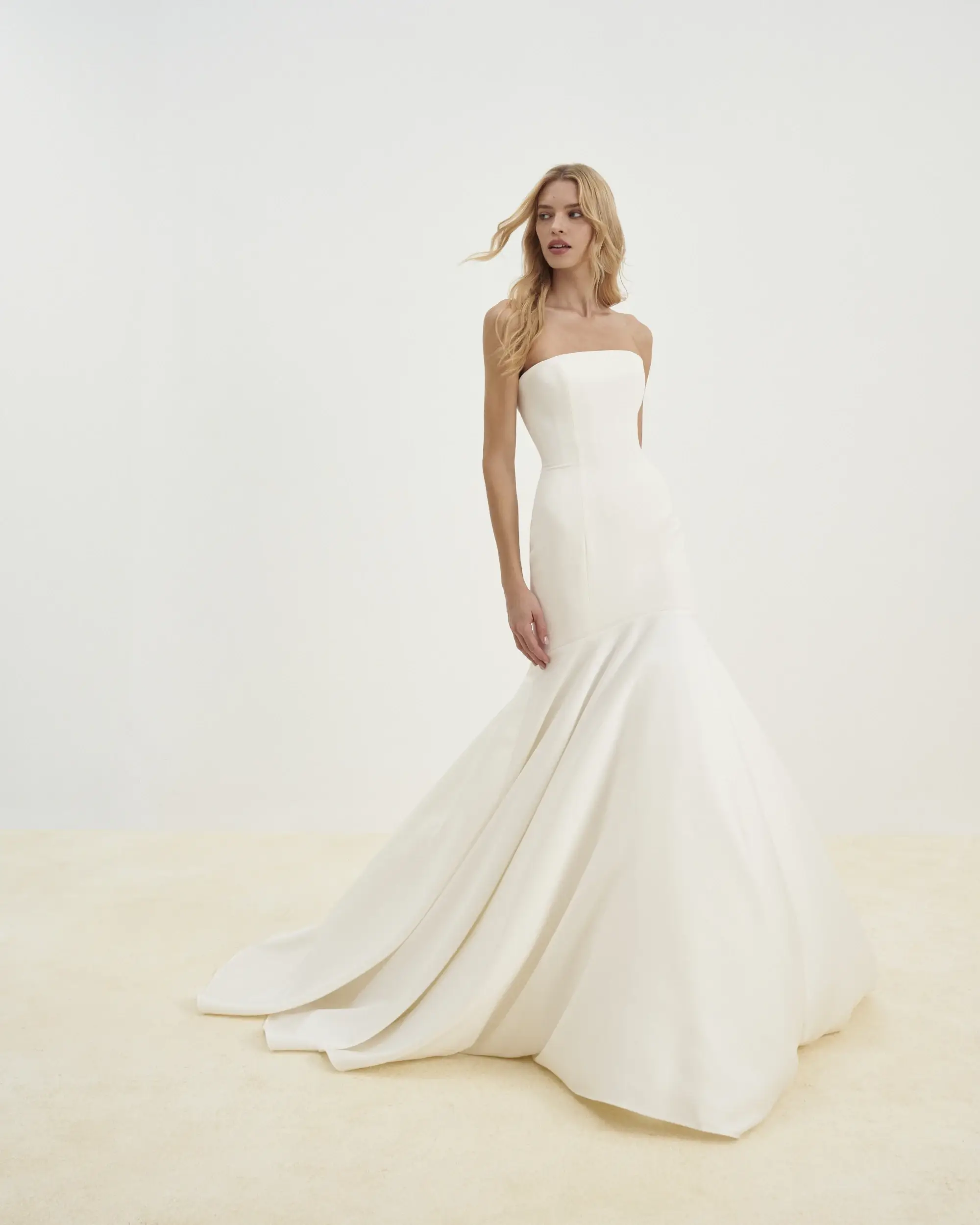 Model is wearing a strapless mermaid gown featuring elegant button detailing down the back