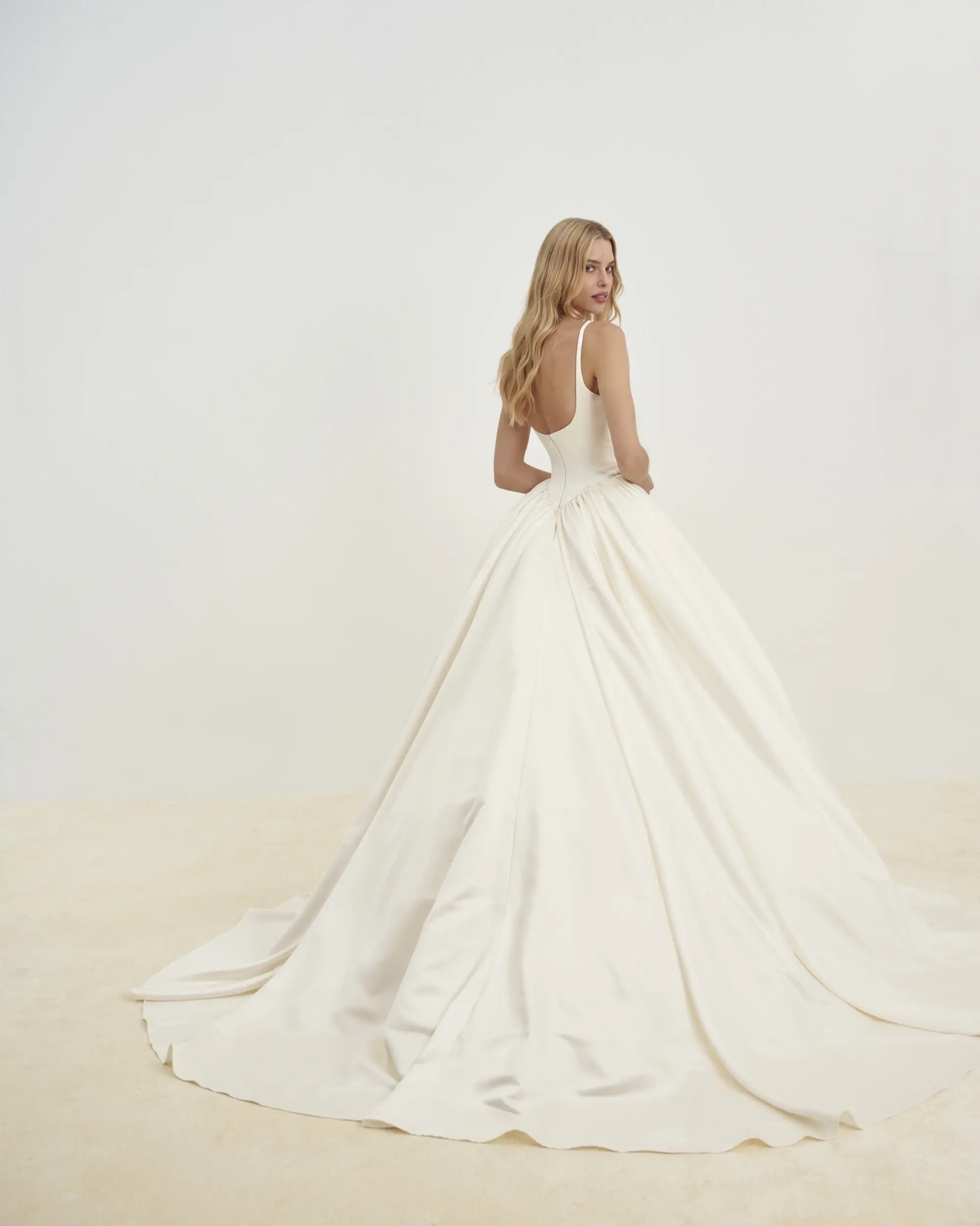 Model is wearing a satin ballgown with delicate sleeveless straps and a Basque waist