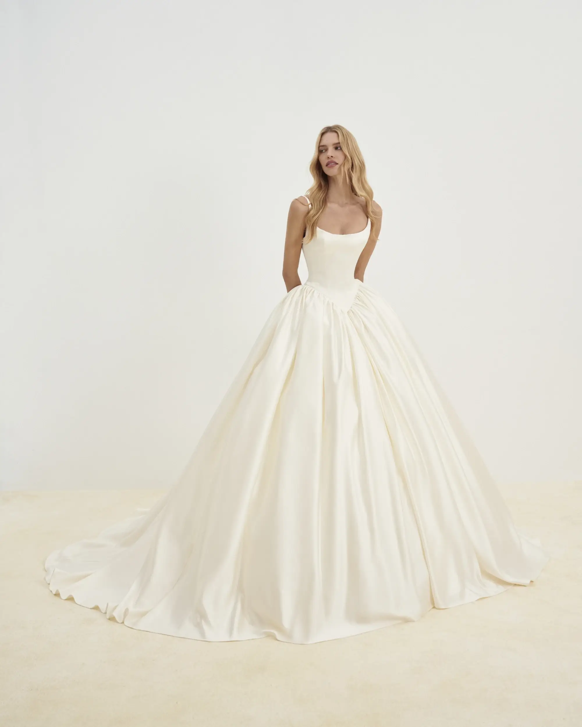 Model is wearing a satin ballgown with delicate sleeveless straps and a Basque waist