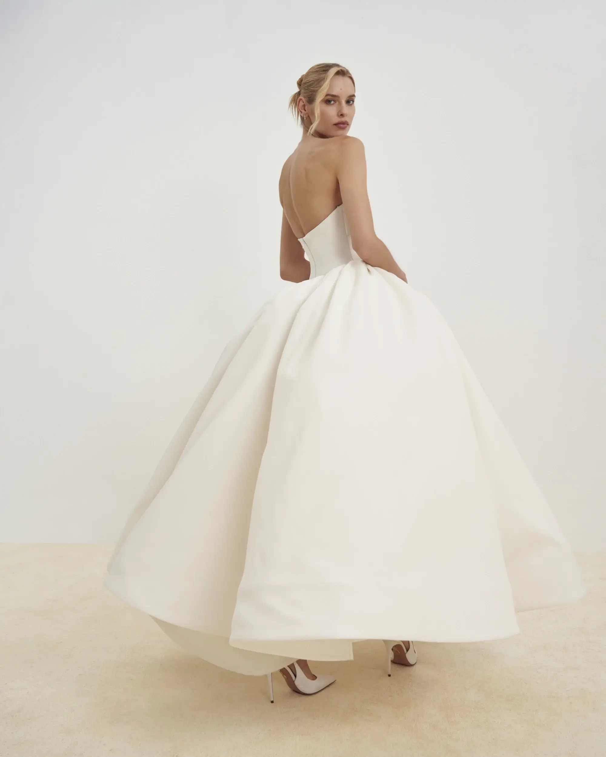Model is wearing a strapless matte Mikado tea-length dress with a flattering Basque waist