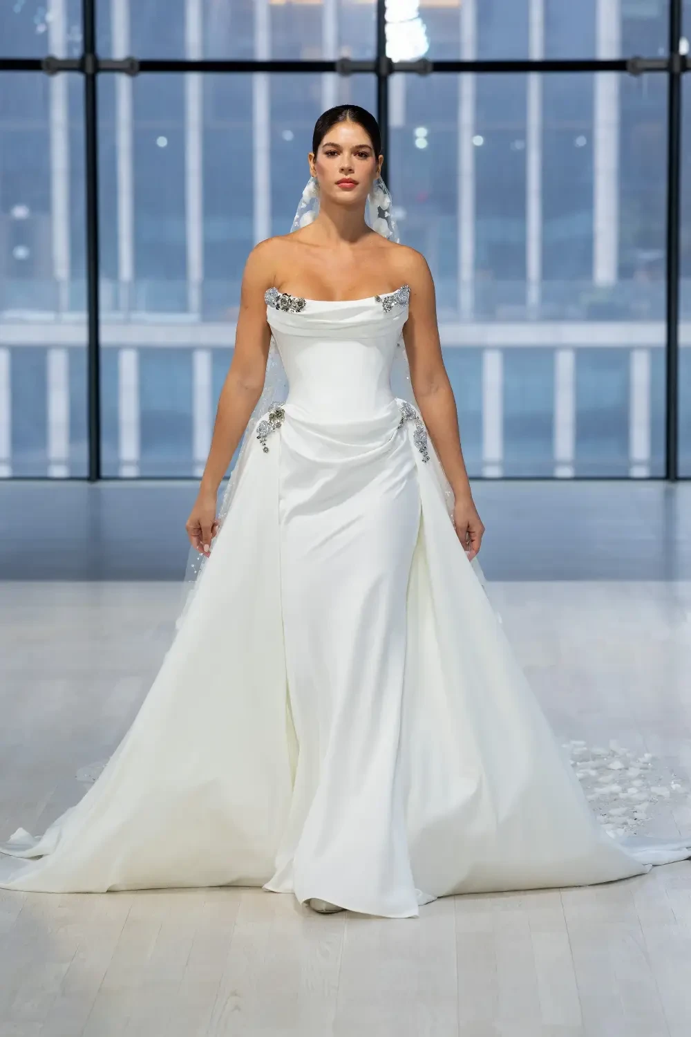 A model walks down the runway wearing a white wedding dress with decorative embellishments.