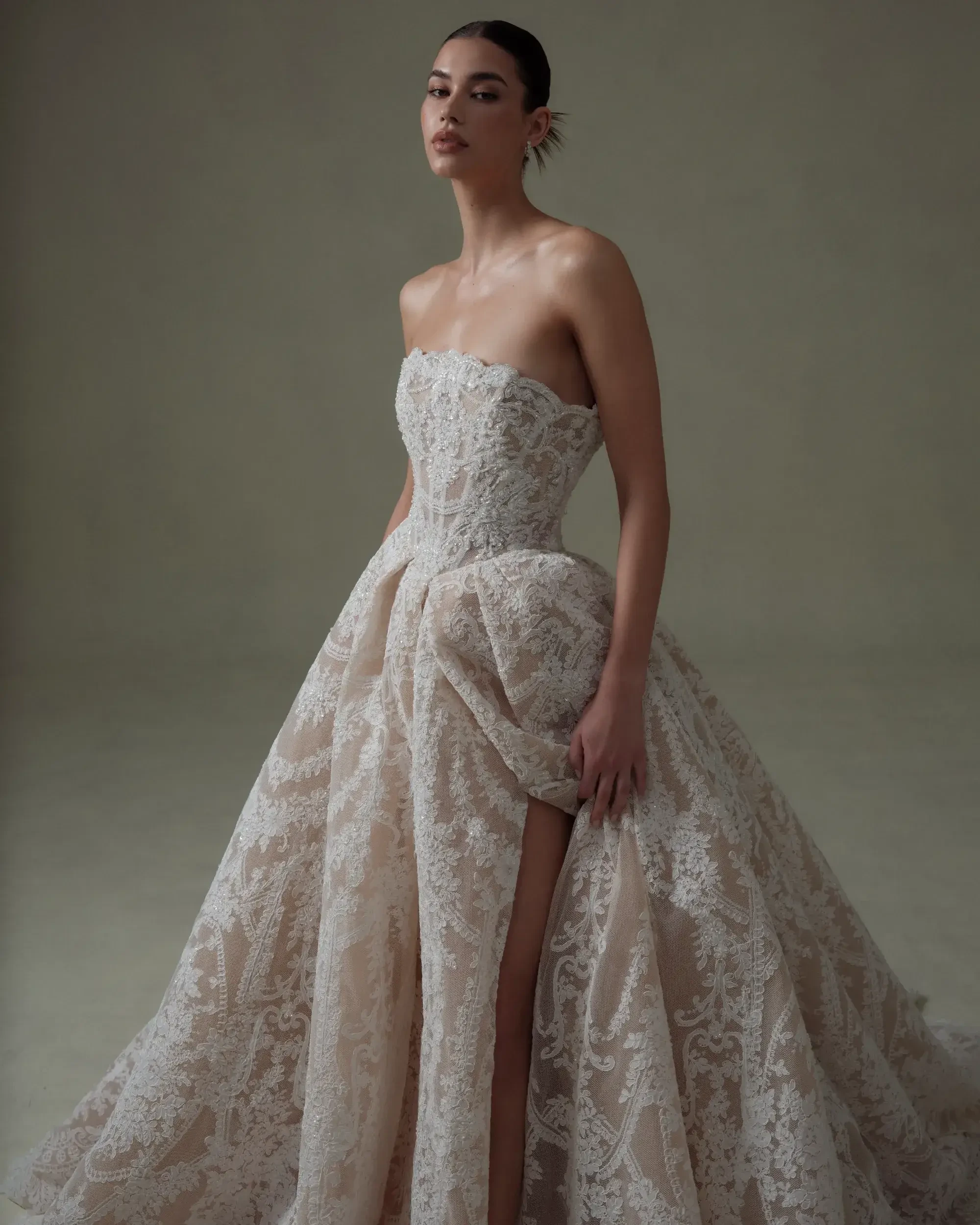 A model wearing a strapless, elegant gown with intricate lace details and a voluminous skirt.
